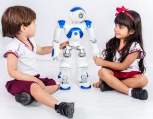 Duas crianças com uniforme do Eficácia (um menino e uma menina) interagem com um robô branco e azul utilizado, normalmente, em aulas de robótica educacional.